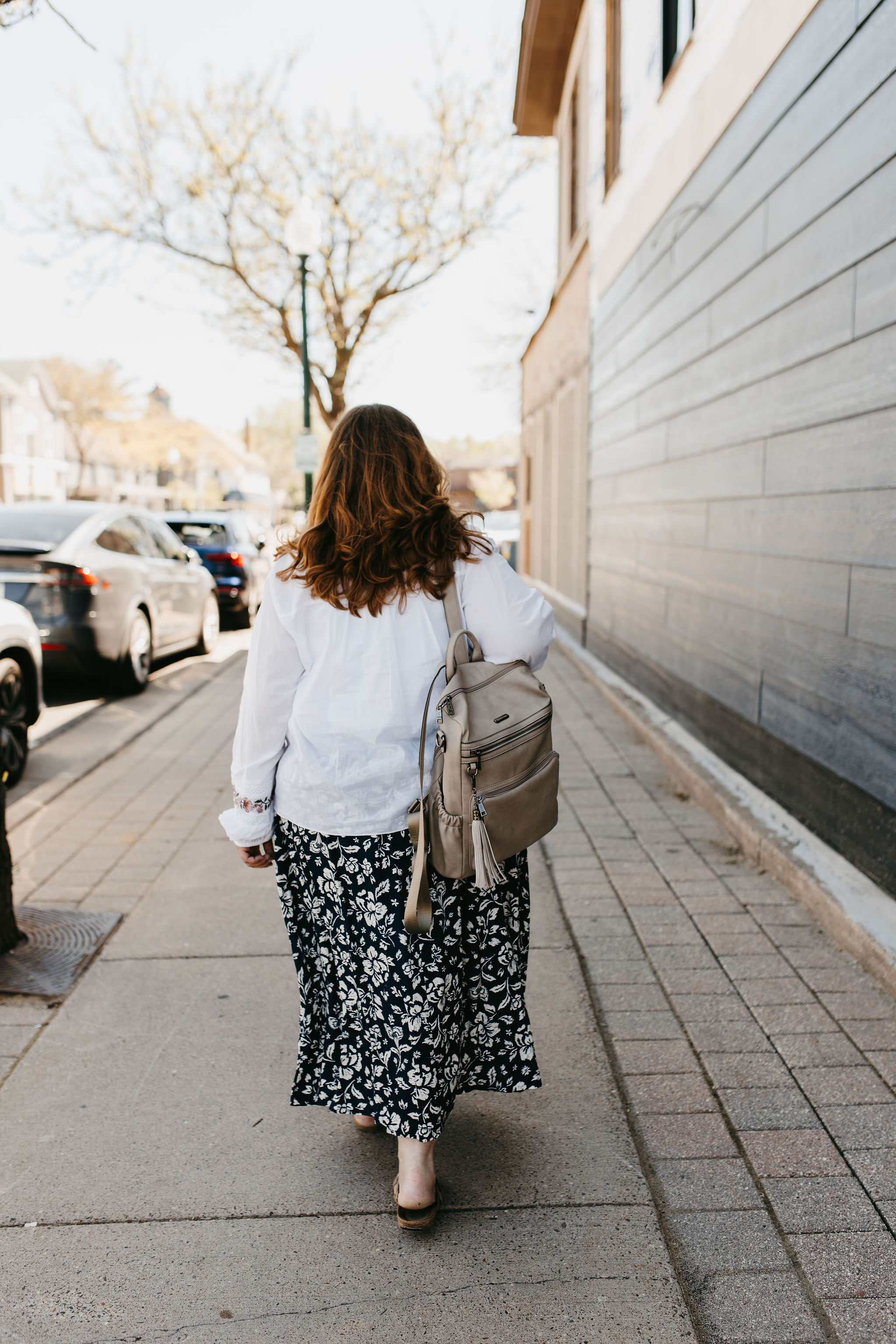 woman with dark reddish hair in white blouse with floral black skirt walking outside