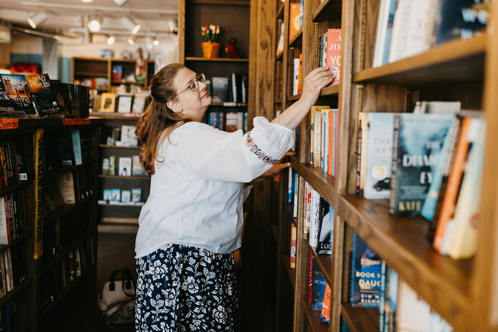 woman with reddish brown hair looking at books white blouse and black floral skirt