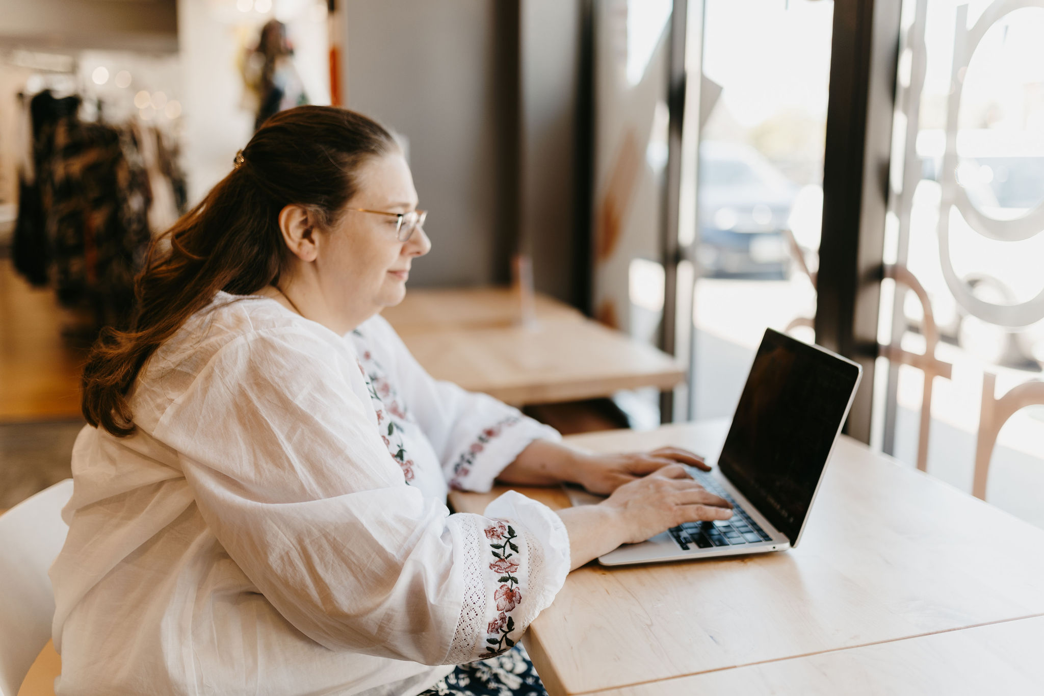 woman with dark hair working on laptop in white blouse