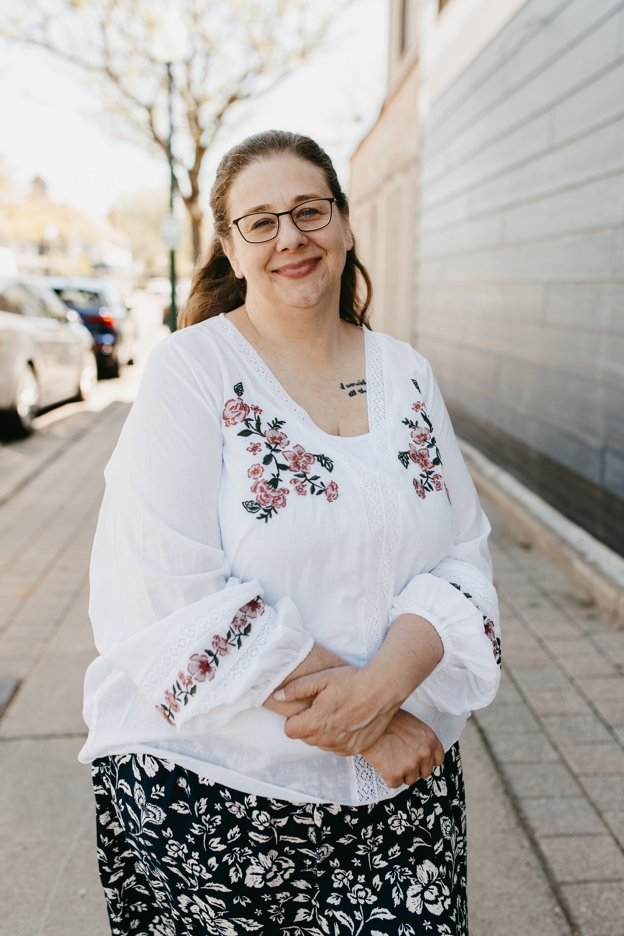 woman with dark hair outside in white floral blouse