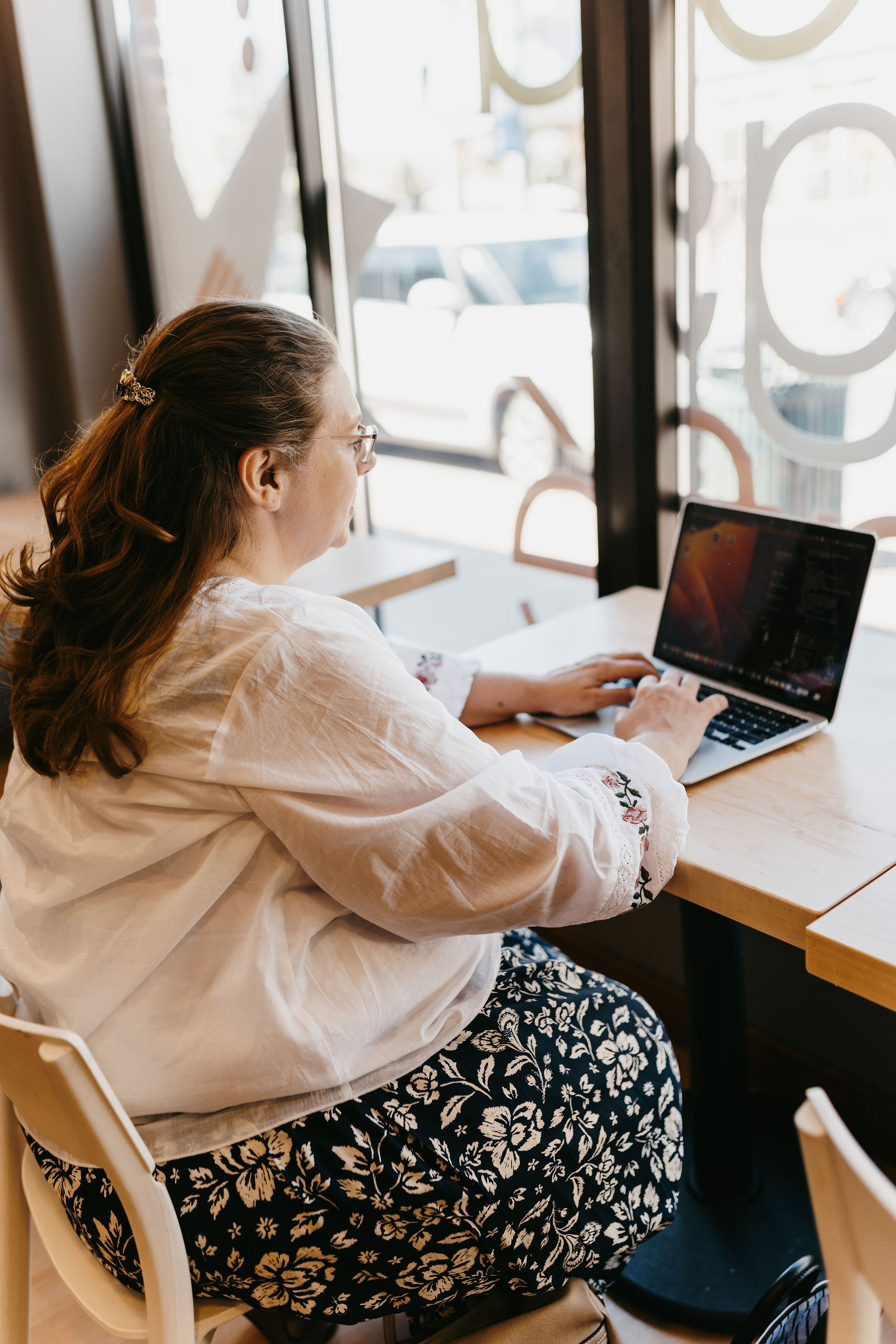 woman with dark hair working on laptop in white blouse
