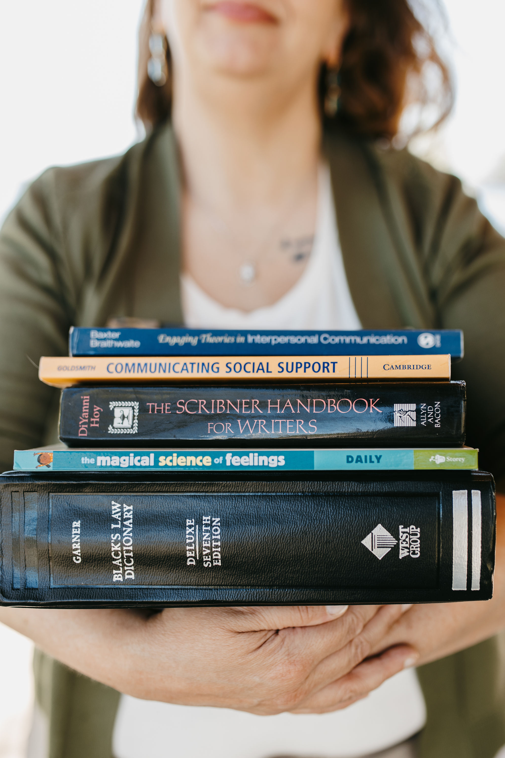 woman with dark hair in white shirt with green cardigan holding law textbooks